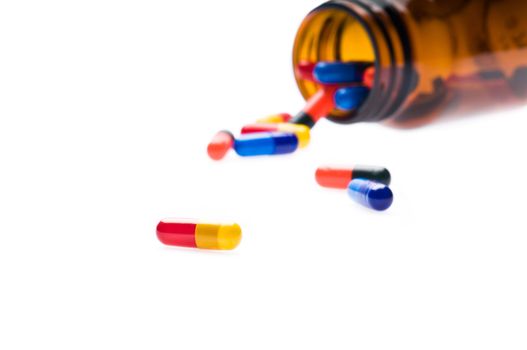 Open pharmaceutical bottle which spills colored capsules over white