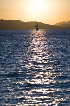 sailboat bathed in dawn sunlight whereby the sun produces nice reflection in the ocean