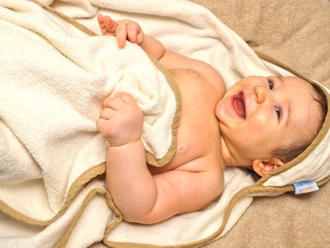 Laughing baby laying on it's back, in a towel