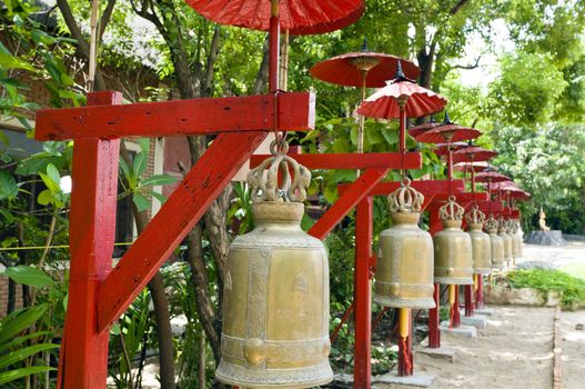 Row of bells in a temple covered by red umbrella on a sunny day