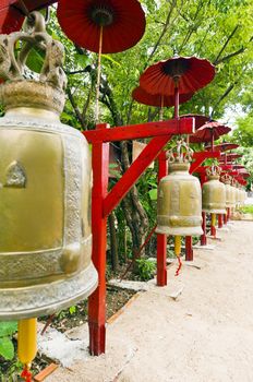 Row of bells in a temple covered by red umbrella on a sunny day