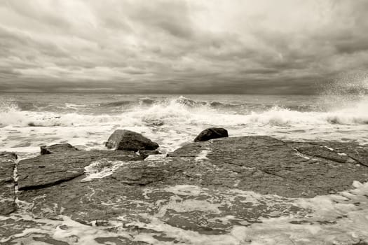 Oceanscape with waves breaking on a rocky coastline under an overcast stormy sky