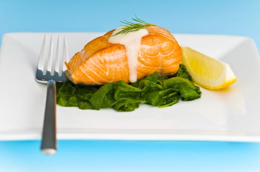 Salmon steak on spinach, decorated with lemon, sauce and fork