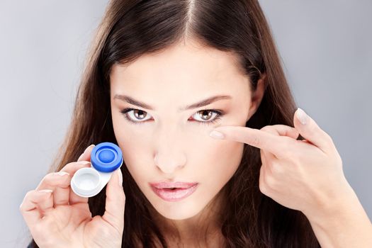 Young woman holding contact lenses cases and lens in front of her face