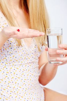Red capsule in woman's hand and glass of water, vertical shoot