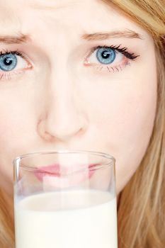expression of a blond girl with blue eyes holding glass of milk and do not like to drink it