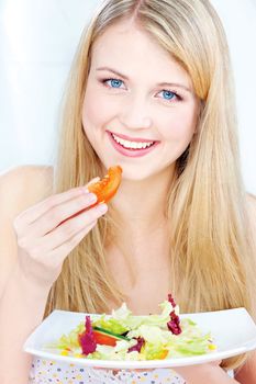 Pretty blue eyes woman eating tomato and holding salad on plate