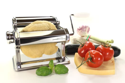 Noodle dough in a pasta machine with tomatoes, zucchini, oil and basil