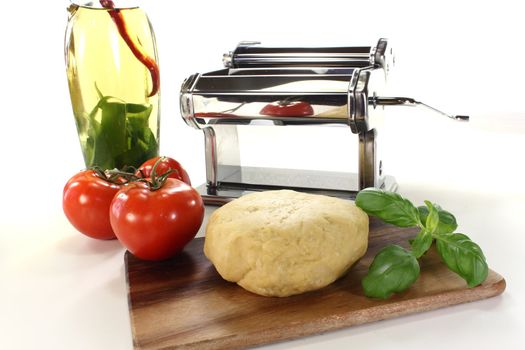 Noodle dough in a pasta machine with tomatoes, oil and basil