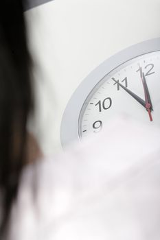 Woman watching the minutes pass on a clock at her desk waiting.