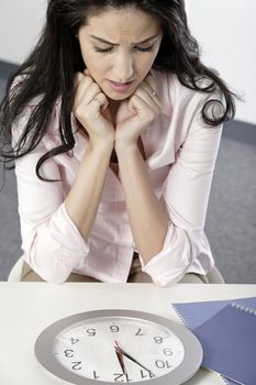 Woman watching the minutes pass on a clock at her desk waiting.