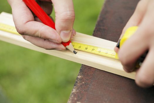 Closeup of carpenter measuring 15 centimeters from slat of wood outdoors.