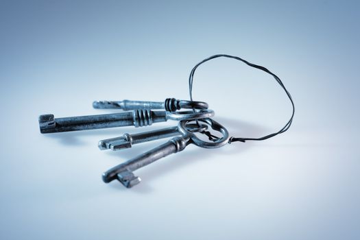 A Blue-toned image of Old antique keys in a key ring made of metallic wire.