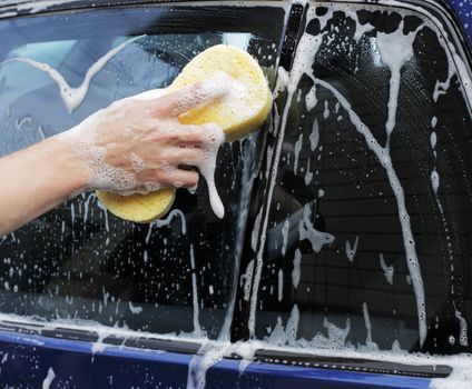 Man washing a car with a yellow sponge.