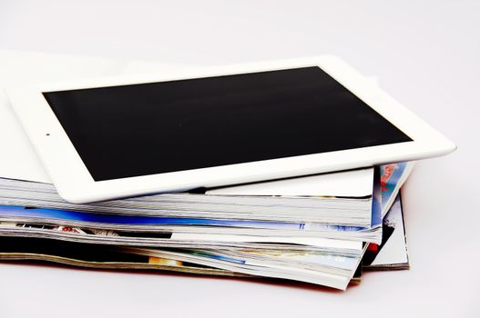 A white tablet on top of a stack of magazines and books