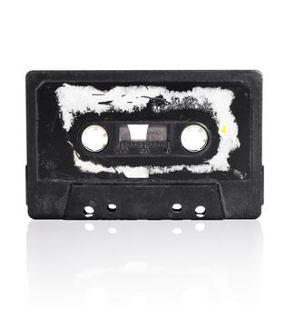 Old black compact audio cassette with torn label isolated on white with natural reflection.