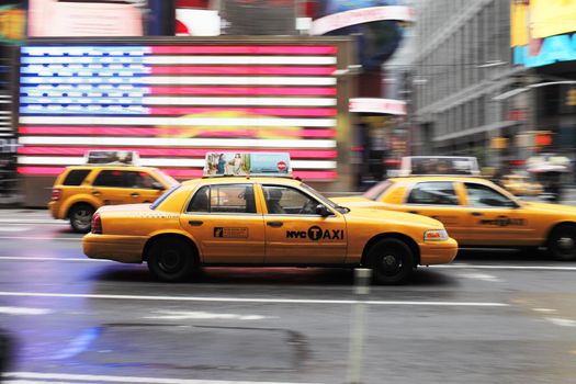 NEW YORK CITY, USA - JUNE 12: Yellow taxi cab speeding through Times Square. A US flag in the background. June 12, 2012 in New York City, USA