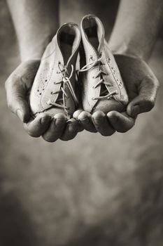 Dirty hands holding a pair of baby shoes. Very shallow depth of field.