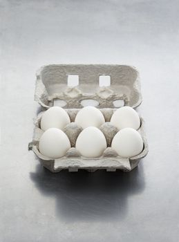 An egg carton with six white eggs on metallic surface.