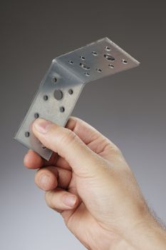 Man holding a 90� metallic angle bracket in his hand.