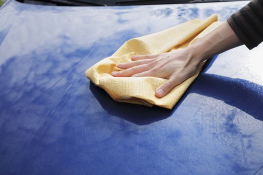 A Hand drying a blue car with a synthetic chamois leather.