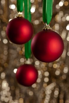 Three red Christmas baubles in front of a gold glitter background for Christmas or decoration
