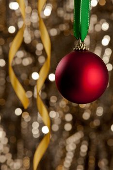 Single red Christmas bauble in front of a gold glitter background for Christmas issues