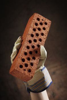 A gloved hand holding a perforated brick