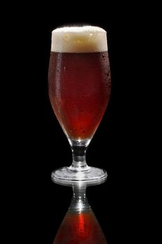 Dark beer in a footed glass on reflective surface.