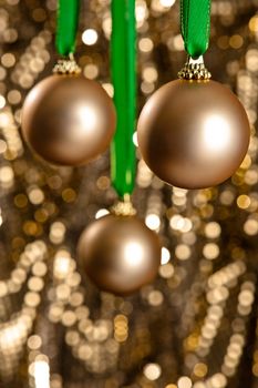 Three golden Christmas baubles in front of a gold glitter background for Christmas or decoration