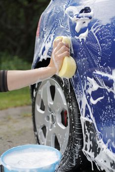 A Hand washing a blue car with a sponge