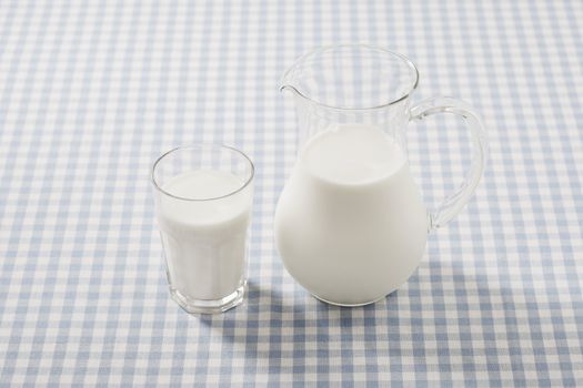 Milk in a glass and a glass pitcher on a plaid tablecloth