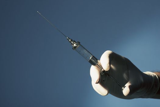 A Gloved hand holding an old glass syringe