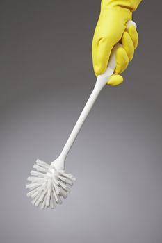 A clean toilet brush held by a hand with yellow rubber glove