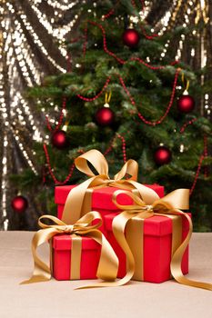 Three presents with gold ribbon, in front of a Christmas tree