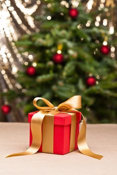 One present with gold ribbon, in front of a Christmas tree