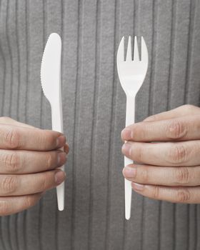 Man holding white disposable cutlery. Knife and fork.