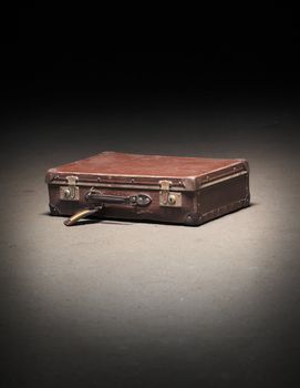 Old worn brown suitcase on dirty concrete floor