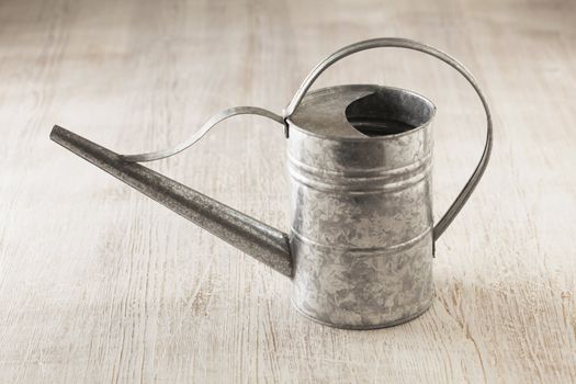 Metallic watering can on wooden surface