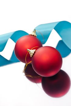 Red Christmas baubles and a blue ribbon on a silver reflective surface 
