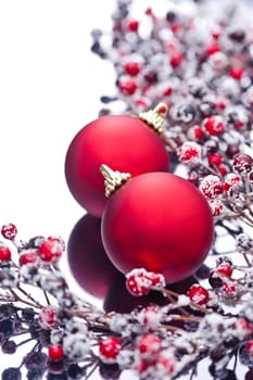 Two Christmas baubles and holly berries on a silver reflective surface 