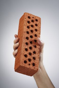 A hand holding a red perforated brick