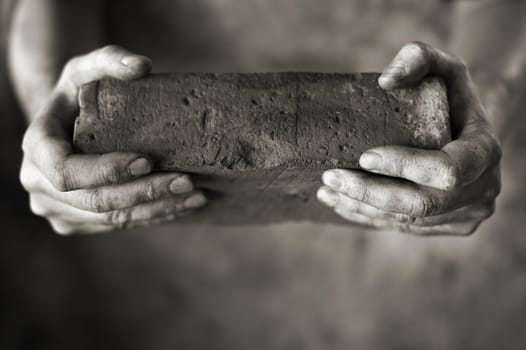 Sepia toned photo of DIrty hands holding an old brick