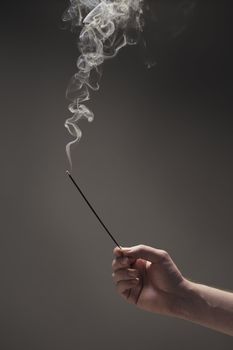 Hand of a man holding a burning incense stick.