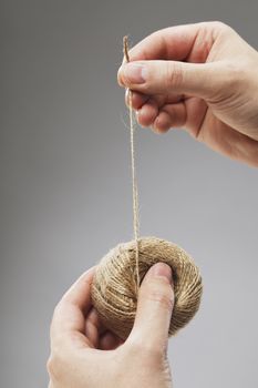 Hands holding a roll of string made of natural fibers.