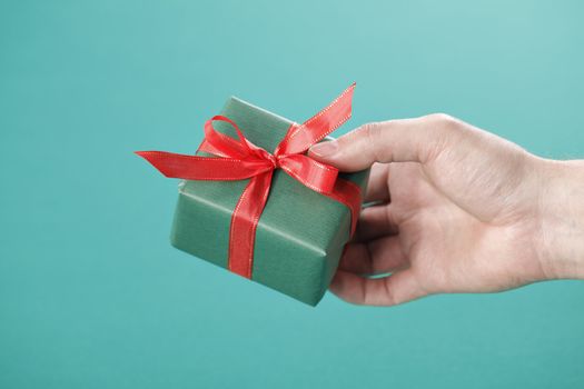 Hand holding a small green gift with red ribbon.