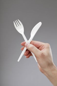 Hand holding white disposable plastic fork and knife