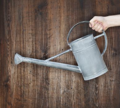 Man holding a metallic watering can against wooden background