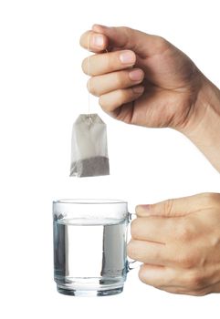 Hand putting a tea bag into a transparent glass cup of hot water