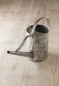 Metallic tin watering can on wooden surface